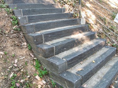 Koyu gri, ahşap desenli bloklar ve beton kaldırımlardan yapılmış, yerdeki kuru yapraklar ve yeşil lahanalarla çevrili açık hava merdivenleri doğal ve kırsal bir yol oluşturuyor..
