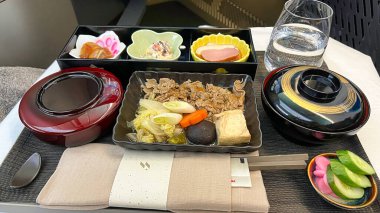 Biftek, sebze ve küçük aperatifler de dahil olmak üzere çeşitli yemeklerle dolu güzel bir uçuş yemeği tepside bir bardak suyla servis edilir..