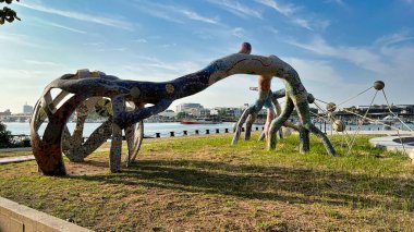 Sarmaş dolaş kökler şeklinde canlı, mozaik kaplı bir kamu sanatı heykeli, Tainan, Tayvan 'da su üzerinde görünen tekne ve binaların bulunduğu çimenli bir bölgede duruyor..