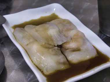 Beyaz dikdörtgen bir tabakta kahverengi soslu haşlanmış karides pirinçlerinin yakın plan görüntüsü..