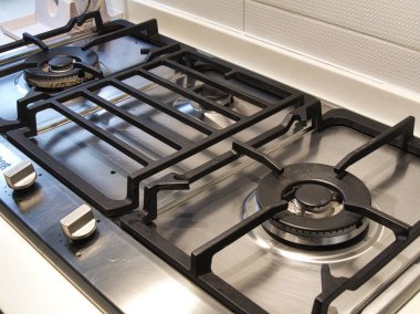 Üç ocağı ve demir ızgarası olan modern bir gaz sobasının yakın çekim görüntüsü fayanslı bir mutfak zeminine kurulmuş..