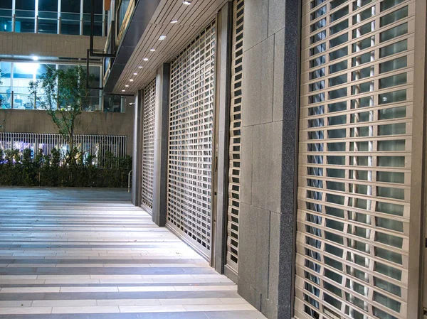 Kapalı metalik paten panjurları ve çizgili kaldırımı olan modern bir bina cephesi..