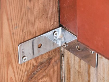 Galvanizli çelik köşe desteğinin yakın plan çekimi. Filipinli baş vidaları ahşap çerçeveye ve yapısal destek ve inşaat desteği için kırmızı boyalı yapıya bağlanmış..