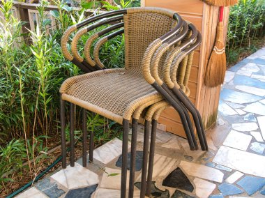 Yeşil bitkilerin yakınındaki taş bir mozaik avluda oturan birkaç tane örülmüş rattan tarzı açık hava sandalyesi..