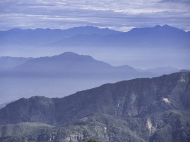 Puslu mavi dağların katmanları, yumuşak bir sabah gökyüzünün altında solup gidiyor, sakin bir izolasyon hissi uyandırıyor ve doğanın el değmemiş geniş çaplı vahşi doğası.