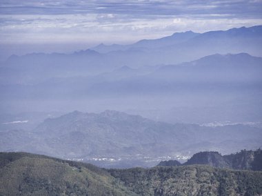 Yoğun bir sabah sisinin içinden katmanlı mavi dağ zirveleri yükselir ve sonsuz bir sükunet ve doğa harikası hissi uyandıran dingin ve ruhani bir manzara yaratır..