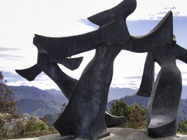 Bir grup bronz heykel uçsuz bucaksız bir dağ manzarasına karşı dans ediyor. Parlak, geniş bir gökyüzü altında insan bağlantısını ve özgürlük ruhunu simgeliyor..