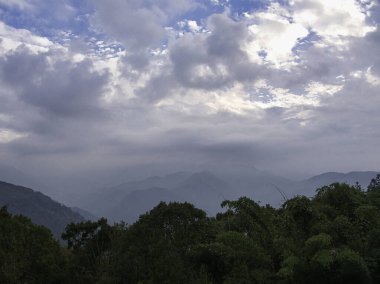 Sakin bir dağ sırası bulutlu bir ufka doğru uzanır. Yoğun yeşil ormanlar sisli tepelerin önünü kaplar. Sabahın erken saatlerinde dinginlik hissi uyandırır..