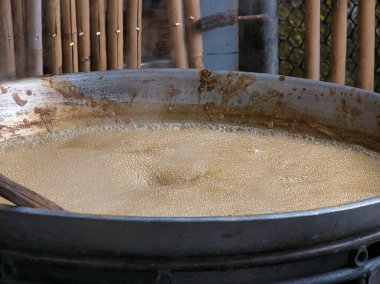 Büyük bir metal tava, taşra mutfağında köpüren kahverengi palmiye şekeri şurubuyla kaynıyor. Geleneksel zanaatkar pişirme yöntemleri ve yerel mutfak mirası sergiliyor..