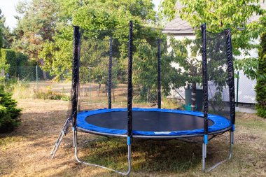 Arka bahçesinde güvenlik ağı olan bir trambolin. Bahçedeki trambolinin önü. Trambolin atlama.