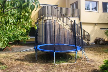 Arka bahçesinde güvenlik ağı olan bir trambolin. Bahçedeki trambolinin önü. Trambolin atlama.