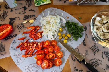Slicing vegetables on cutting board. Homemade  salad. Chopped onions,red peppers,tomatoes,dill, olives and feta cheese.