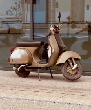 Bir binanın önüne park etmiş eski güzel bir scooter yeni bir araba için sahibini bekliyor.