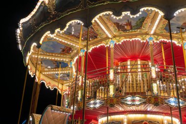 Gdansk, Polonya - 25 Kasım 2024 Akşam gökyüzünün altında sıcak ışıklarla parlayan klasik bir atlıkarınca. Kırmızı ve altın elementli geleneksel panayır eğlencesi şenlik neşesini yansıtıyor. Noel pazarlarını tasvir etmek için harika