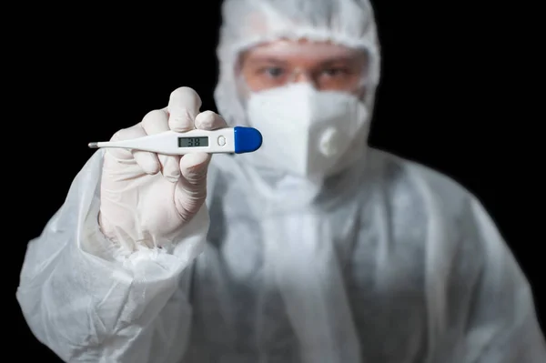 Koruyucu kıyafetli, maskeli, gözlüklü bir doktor siyah arka planda elektronik termometre tutuyor. Salgın, Coronavirus covid 19 salgını. Sıcaklık ölçülüyor ve gösteriliyor