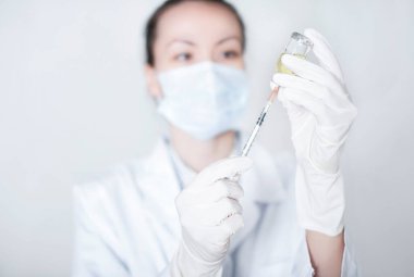 Genç hemşire beyaz arka planda bir şırıngaya ilaç koyuyor. Aşılama kavramı