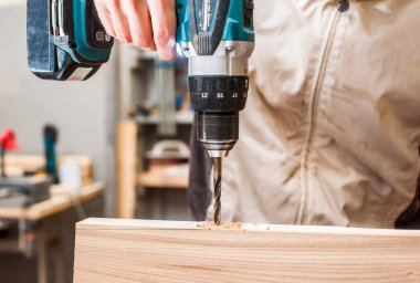 Bir adam, bir marangoz atölyesinde elektrikli matkapla tahtayı deliyor. Yakın plan.