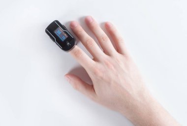 Beyaz arka planda işaret parmağında nabız oksimetresi var. Kan oksijeni ve nabız ölçümü. Yukarıdan bak. Akciğer hastalığı. Kavram