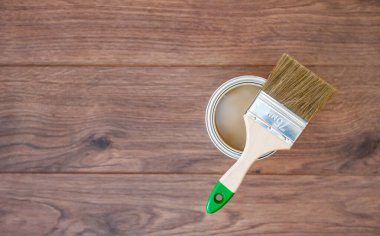 Açık kahverengi boya kutusundaki bir boya fırçası koyu ahşap zeminde yatıyor. Boşluğu kopyala 