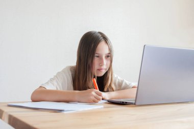 Küçük bir kız evdeki bir bilgisayarda kitap ve defterlerle çalışıyor. Çevrimiçi eğitim, uzaktan öğrenme, karantina. Kavram 