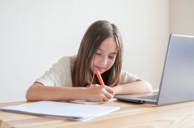 Küçük bir kız evdeki bir bilgisayarda kitap ve defterlerle çalışıyor. Çevrimiçi eğitim, uzaktan öğrenme, karantina. Kavram 