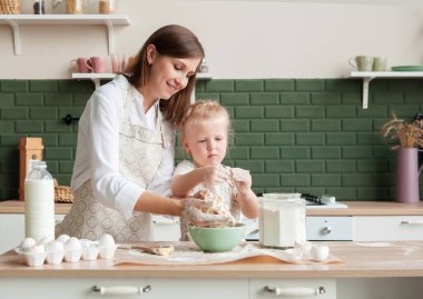 Mutlu anne ve küçük kızı evde, mutfakta hamur yoğuruyorlar. Küçük kız anneme mutfakta yemek pişirmesi için yardım ediyor.