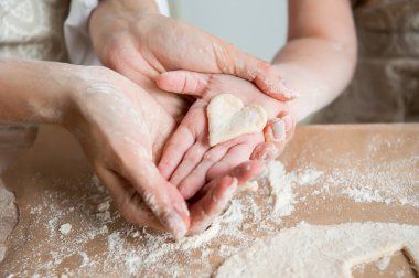 Anne ve kızı hamurdan bir kalp taşıyor. Birlikte mutfakta kurabiye pişiriyorlar. Yakın plan. 