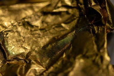 Altın renkli parlak çikolata ambalajının detaylı bir makro fotoğrafı. Yakalayıcı dokular, ışık yansıması ve lüks bir cazibe..