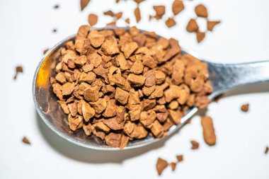 Temiz beyaz bir zemin üzerine yerleştirilmiş koyu kahverengi kahve taneleriyle dolu bir kaşığın detaylı makro fotoğrafı, doku ve aromayı ön plana çıkarıyor..