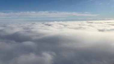 Sakin bir hava fotoğrafı bulutları ve açık gökyüzünü bir uçak penceresinden görüyor, uçuşun güzelliğini ve bulutların üzerindeki huzurlu atmosferi gösteriyor..