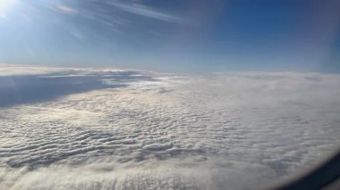 Sakin bir hava fotoğrafı bulutları ve açık gökyüzünü bir uçak penceresinden görüyor, uçuşun güzelliğini ve bulutların üzerindeki huzurlu atmosferi gösteriyor..