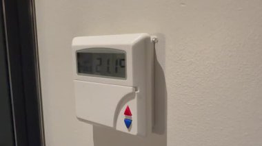 Bir duvara monte edilmiş modern dijital akıllı termostat aktif sıcaklık ayarları ve kullanımda olan akıllı iklim kontrollerini gösterir.