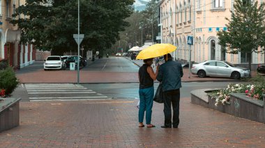 Yağmurlu bir şehir caddesinde şemsiye altında birlikte yürüyen iki kişi. Chernihiv, Ukrayna 21.07.2025