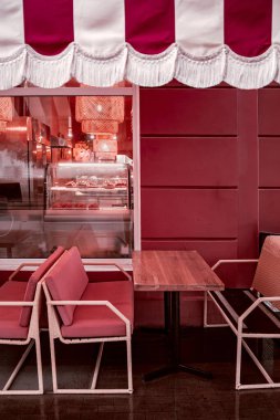 Pembe kafe terası, rahat bir açık hava koltuğu ve sıcak iç ışıkları var. Şık sandalyeler ve ahşap masa kahve molası için davetkar bir ortam yaratır..