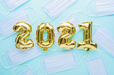 2021 numaralı altın folyo balonları mavi arka planda tıbbi maskeli, Noel, pandemik koronavirüs sırasında yeni yıl, COVID Tatili, pandemik tatil konsepti, üst görünüm, düz yatış