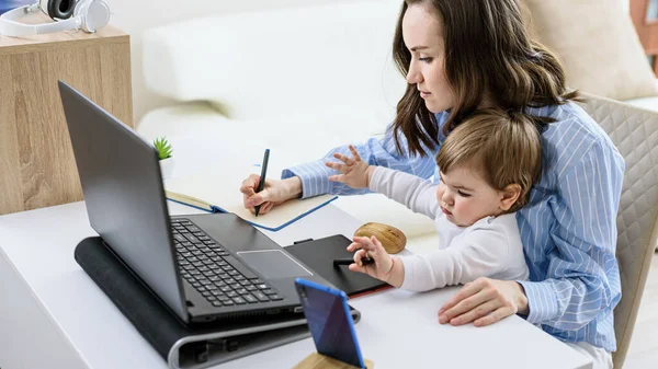 Çocuklu esmer bir kadın dizüstü bilgisayarda oturup not defteri, online kurslar, evde uzaktan çalışma, ev konseptinden çalışma.