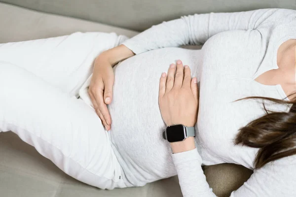 妊娠中の女性がベッドの上で手で腹を抱きかかえて — ストック写真