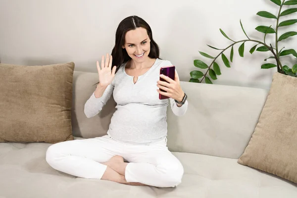 Mujer Embarazada Sonriente Comunica Teléfono Inteligente Mientras Está Sentado Sofá — Foto de Stock