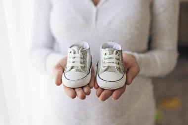 Hamile kadın elinde bebek botları, yakın plan, hamilelik konsepti, beklenti