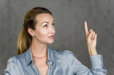 Gülümseyen ve onun parmağı yukarı gösteren gri bir arka plan üzerinde güzel kız