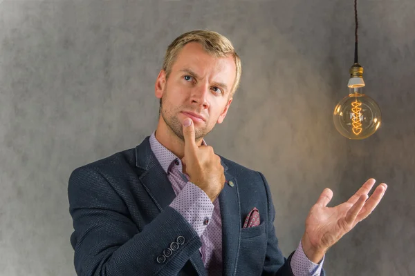 Düşünme işadamı ve gri bir arka plan ve vintage bir elektrik lambaları elini gösterir
