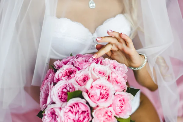 Schöne sexy junge Braut Unterwäsche sitzt auf einem Bett mit einem Blumenstrauß in den Händen und mit einem Schleier auf dem Kopf. Morgen die Braut. — Stockfoto