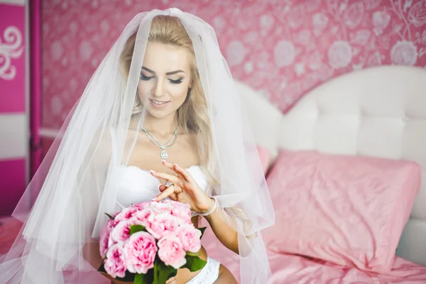 Szép szexi fiatal menyasszony fehérnemű ült egy ágyon, egy-egy csokor virág, kezében, és a fejét a fátyol. Reggel a menyasszony. — Stock Fotó