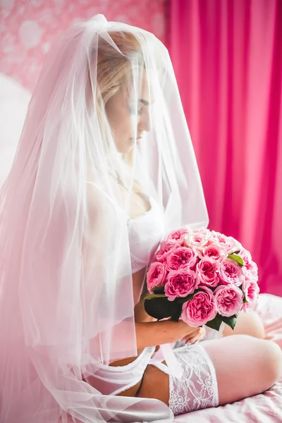 Εσώρουχα όμορφη σέξι νεαρή νύφη που κάθεται σε ένα κρεβάτι με ένα μπουκέτο λουλούδια στα χέρια και με ένα πέπλο στο κεφάλι της. Το πρωί η νύφη. — Φωτογραφία Αρχείου