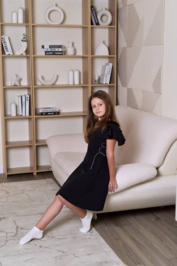 Modern rahat oturma odasındaki kanepede oturan zarif siyah elbiseli bir kızın portresi.