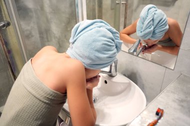 Modern banyo içlerindeki lavaboda başı havluyla yıkanmış bir çocuk.