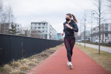 Sokakta maskeyle koşan bir kadın, karantina sırasında spor, koşmadan önce ısınma, kentsel çevre şehrinde