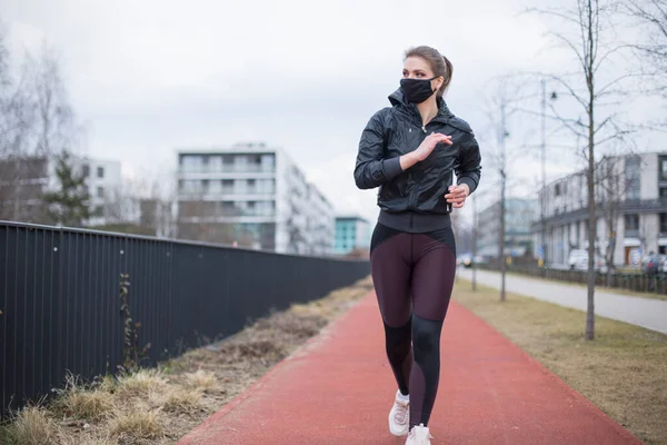 woman running on the street in mask, sport during quarantine, warm-up before running, in an urban environment city