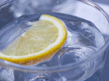Soğuk suyla dolu berrak bir bardak üzerinde yüzen bir dilim limon içerir. Güneş soğuk içecekten yansıyor, ferahlatıcı bir görünüm yaratıyor sıcak hava için mükemmel.