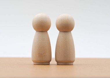 İki basit tahta figür pürüzsüz bir ahşap yüzey üzerinde yan yana yerleştirilmiştir. Doğal ışık, boyanmamış yüzeylerini vurgular. Sıcak ve huzurlu bir atmosfer yaratır.